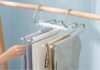 an image of a stainless steel multi-layer pants hanger. It should be hanging in a modern wardrobe filled with various types of garments like pants, scarves, and towels. The hanger should showcase a sleek, space-saving design with up to five horizontal rods, each holding folded clothing. Include a rotating hook at the top, and highlight the detachable rods for easy access. The background should be a neatly organized wardrobe with a minimalist, bright, and clutter-free aesthetic."