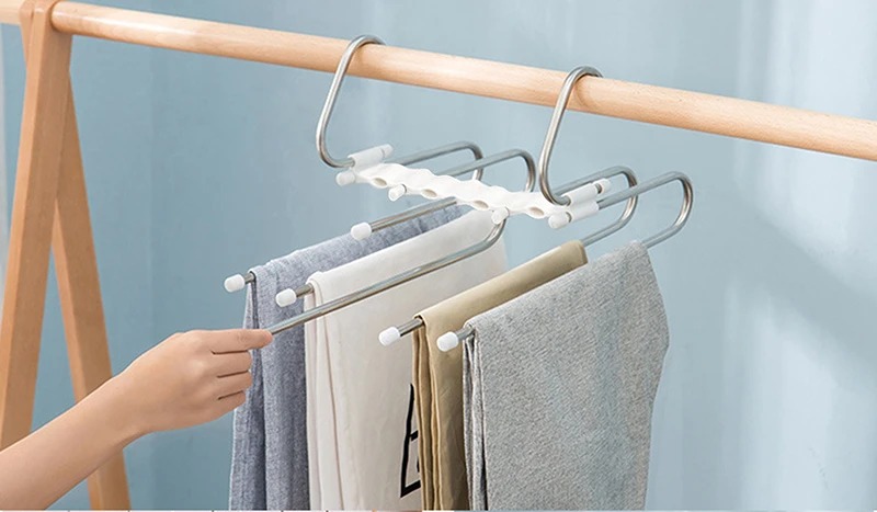 an image of a stainless steel multi-layer pants hanger. It should be hanging in a modern wardrobe filled with various types of garments like pants, scarves, and towels. The hanger should showcase a sleek, space-saving design with up to five horizontal rods, each holding folded clothing. Include a rotating hook at the top, and highlight the detachable rods for easy access. The background should be a neatly organized wardrobe with a minimalist, bright, and clutter-free aesthetic.&quot;